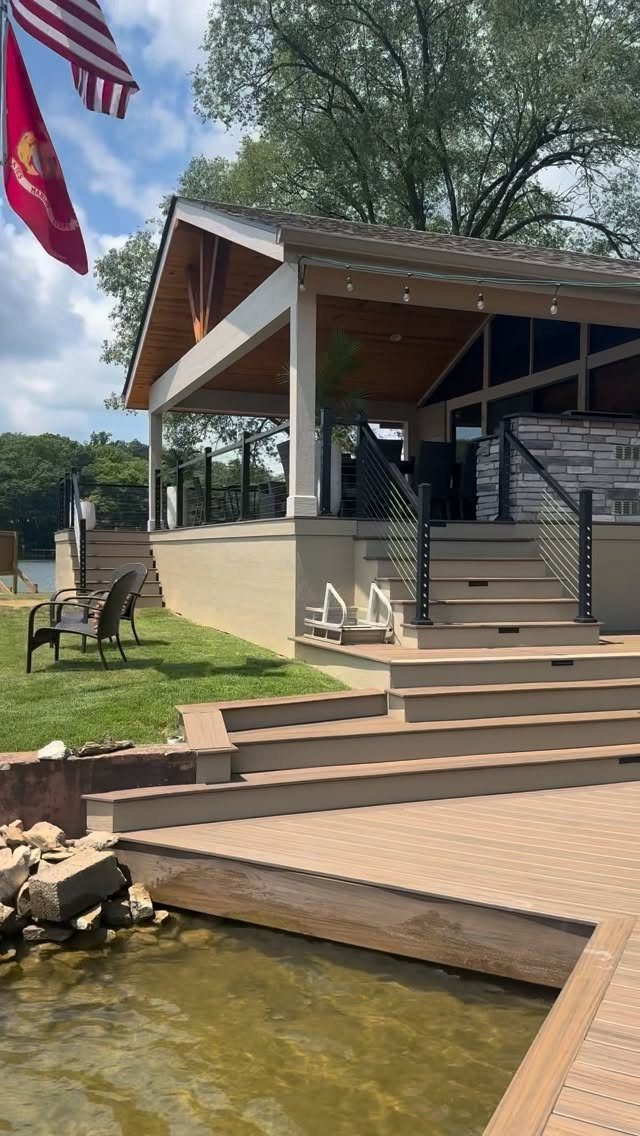 Multi-level wooden deck with a gabled roof and hanging string lights overlooking a body of water.