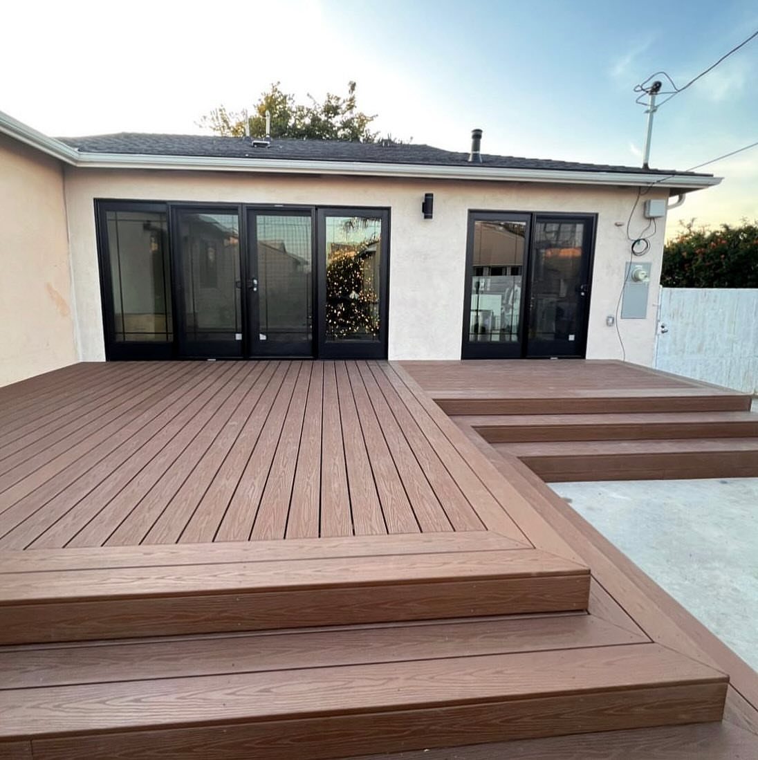 Brown multi-level wooden deck with wide steps leading up to a house with glass doors.