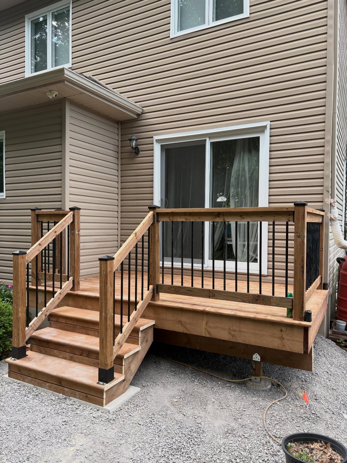 A wooden backyard deck with stairs and black metal railings attached to a tan house.