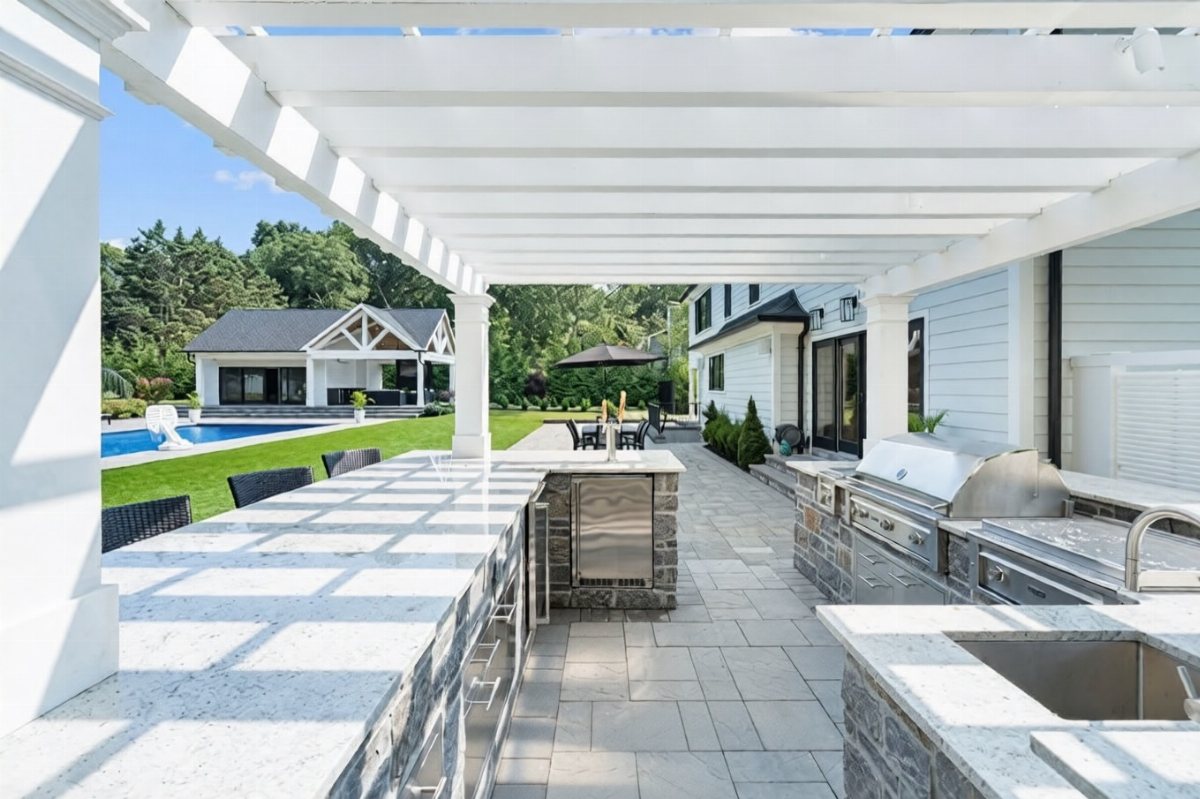Modern outdoor kitchen with granite counters and stainless steel appliances overlooking a backyard pool.