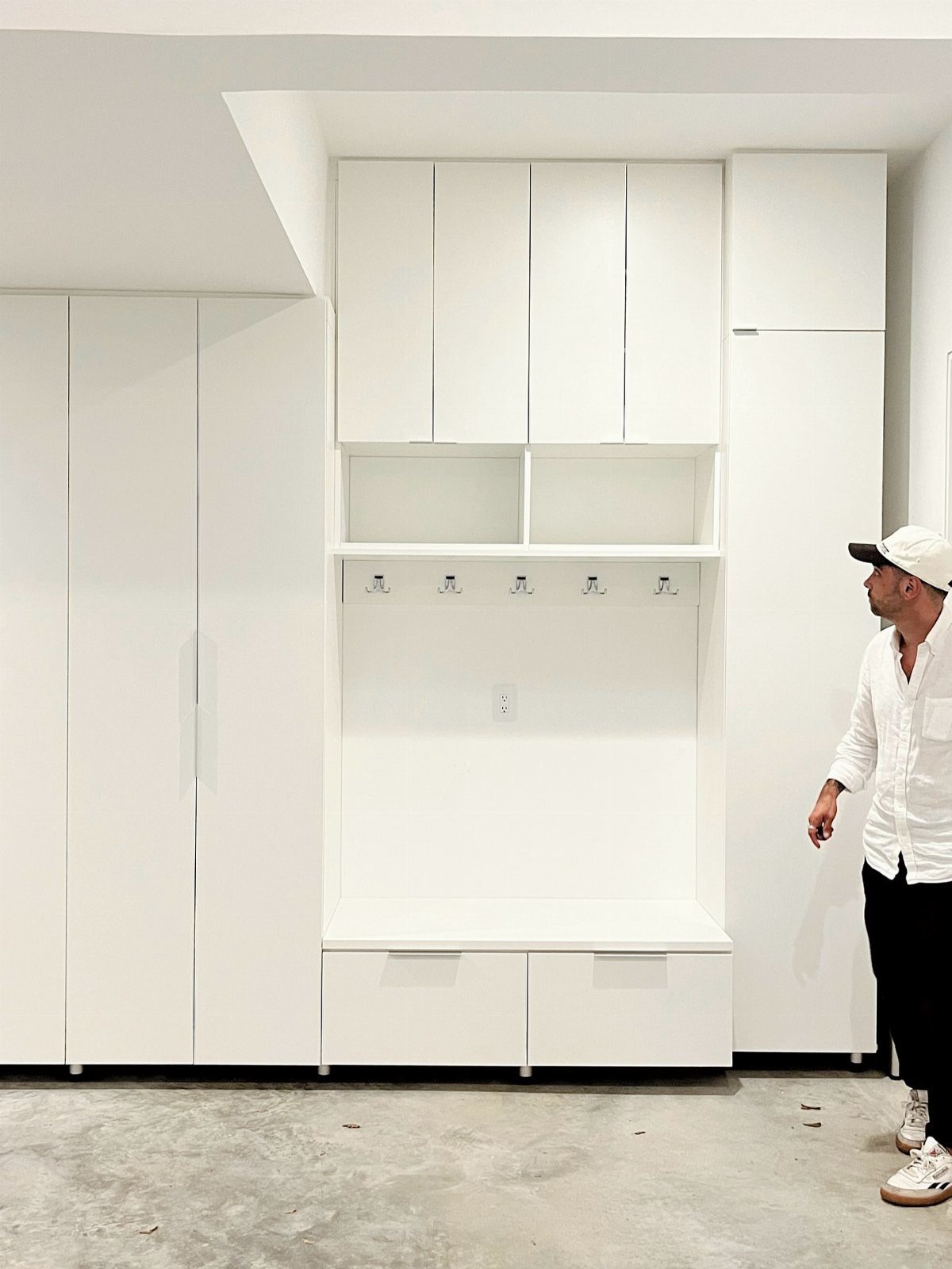 A man standing beside a large white built-in mudroom storage unit with a bench.