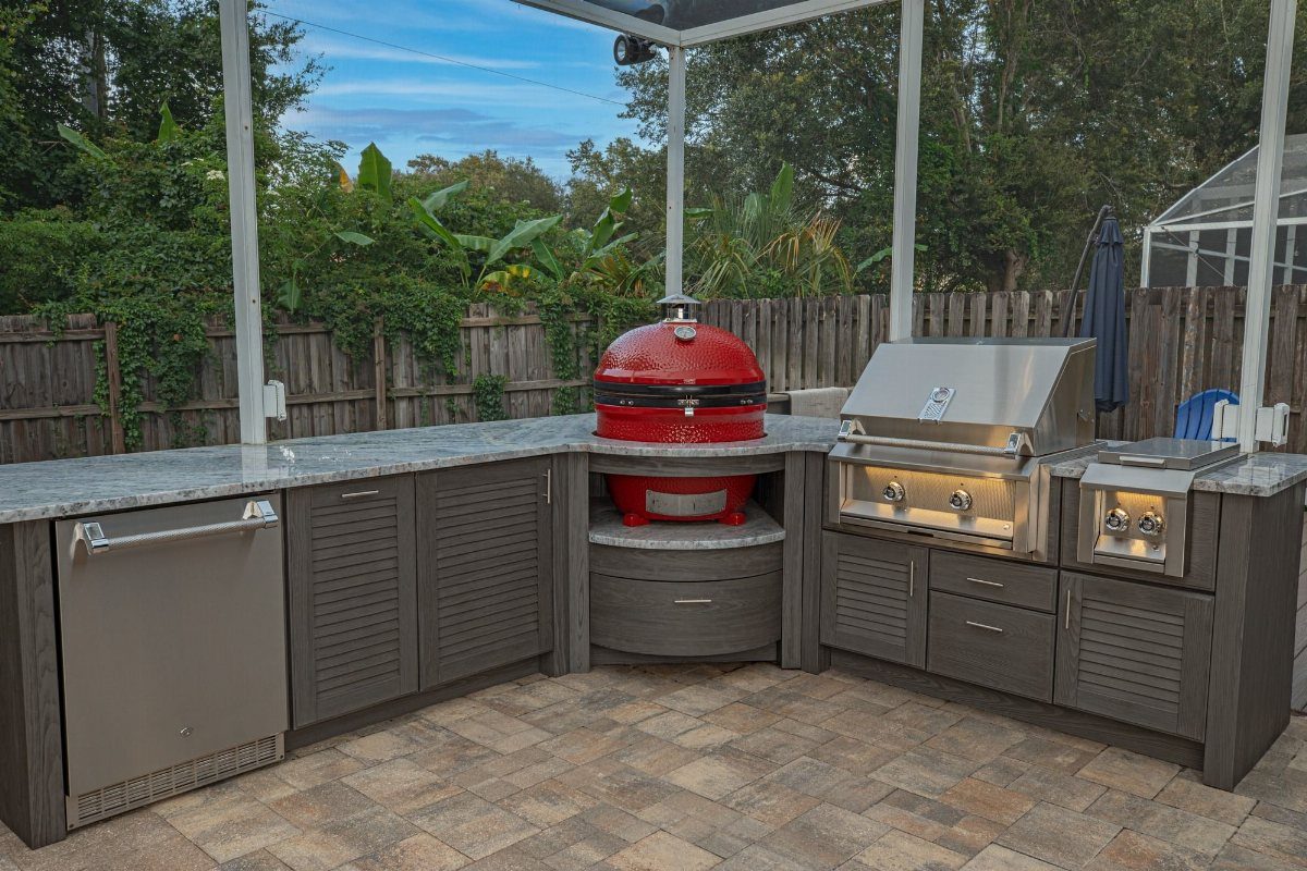 Red ceramic kamado cooker built into a grey outdoor kitchen with granite countertops.