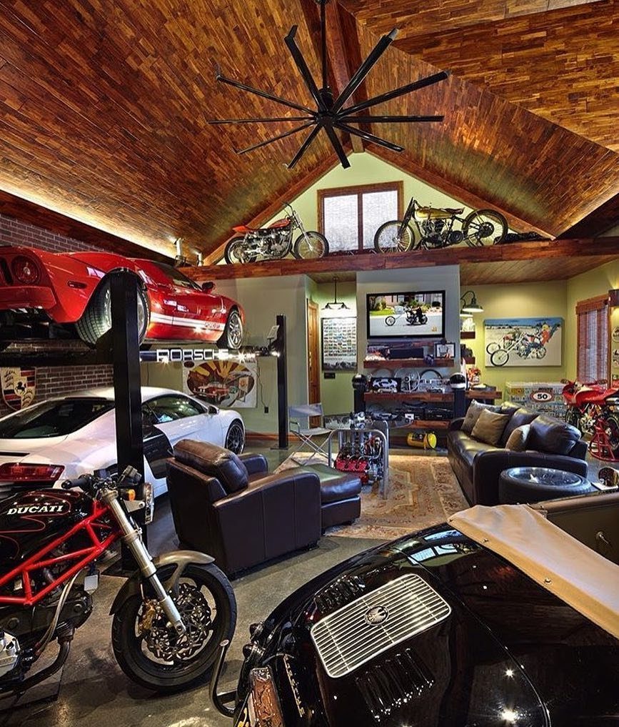 Luxury garage lounge with sports cars, motorcycles, leather seating, and wood-paneled ceilings.