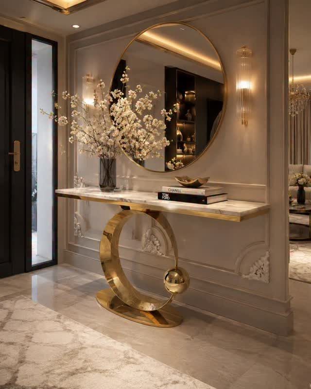 Gold sculptural console table with marble top and round mirror in a living room.