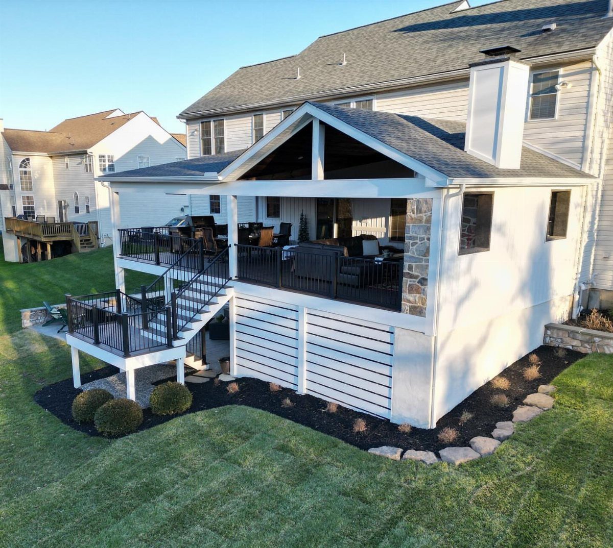 A white two-story deck with black railings and horizontal privacy slats attached to a house.