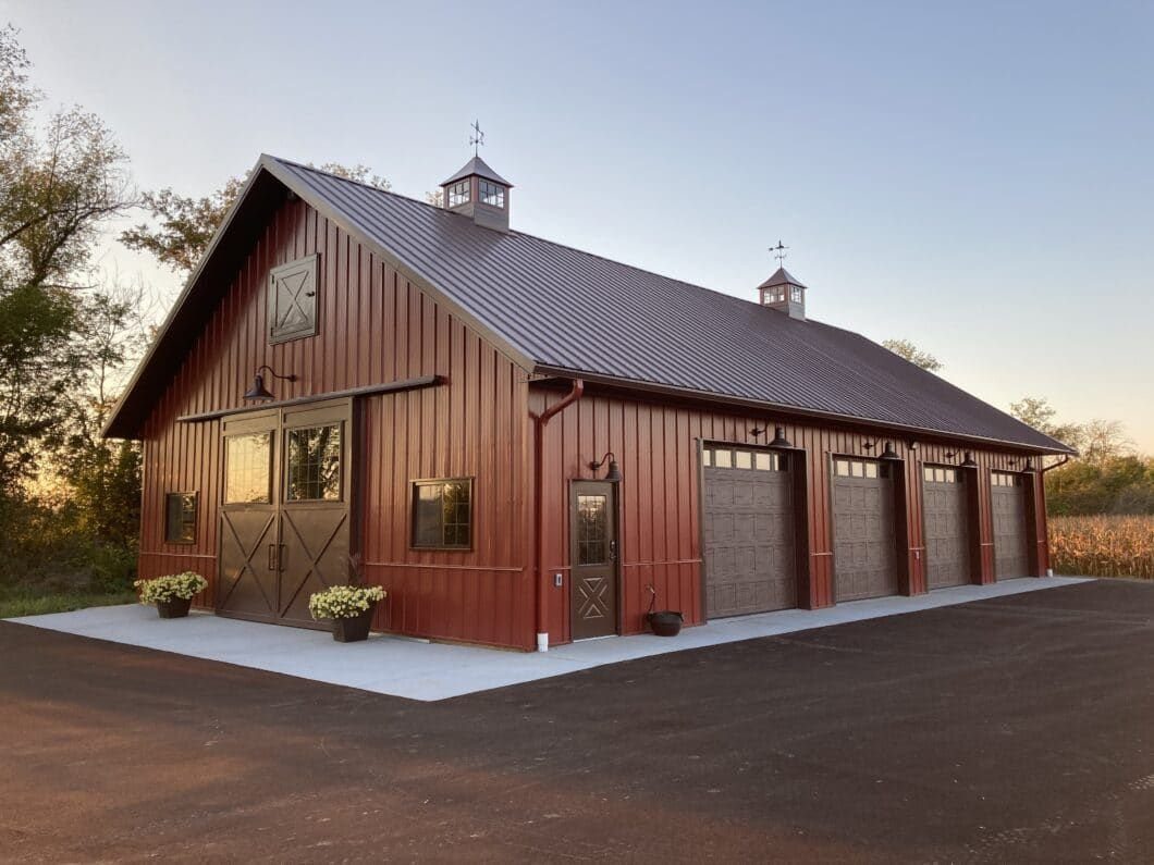 Red pole barn garage with brown metal roof, multiple garage doors, and decorative cupolas.