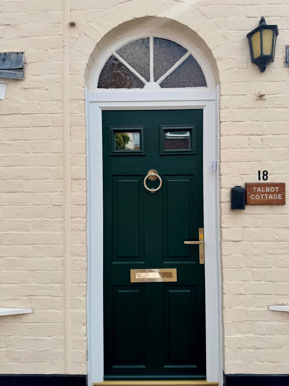 Dark green front door with gold hardware set in a white arched frame against beige brick.