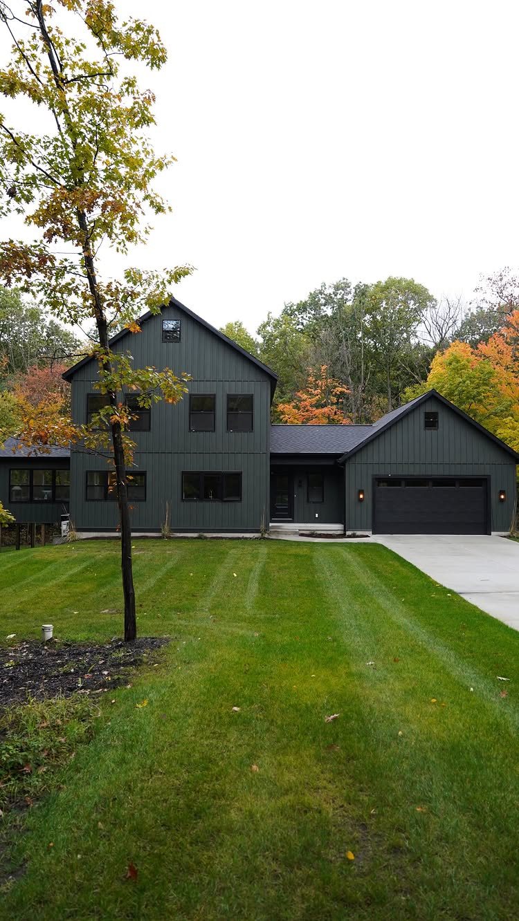 A modern two-story house featuring dark green vertical siding and black accents with a green lawn.