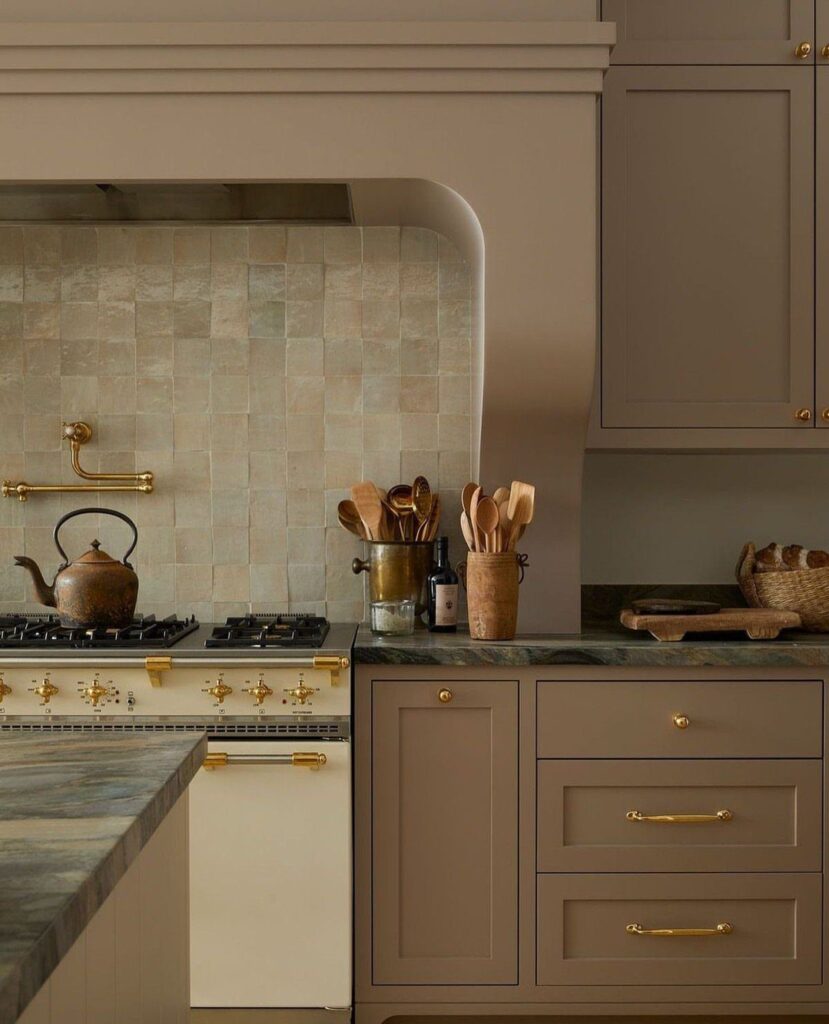 Taupe kitchen cabinets with gold hardware and a dark marble countertop.