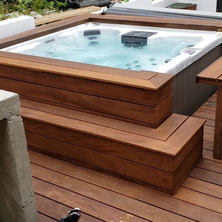 A white hot tub built into a wooden deck with brown timber steps.