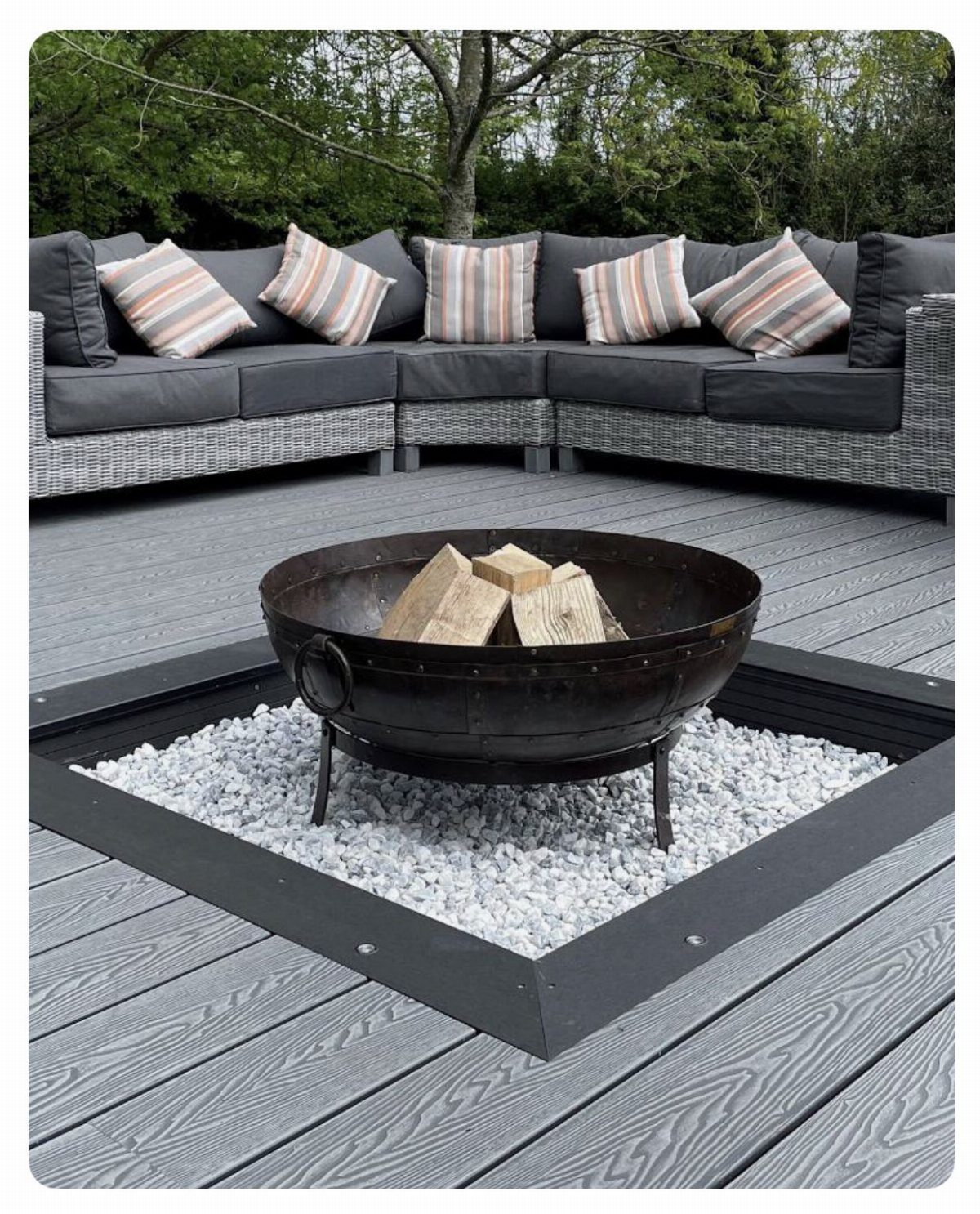 Metal fire bowl with wood on white stones set into a grey composite wood deck.