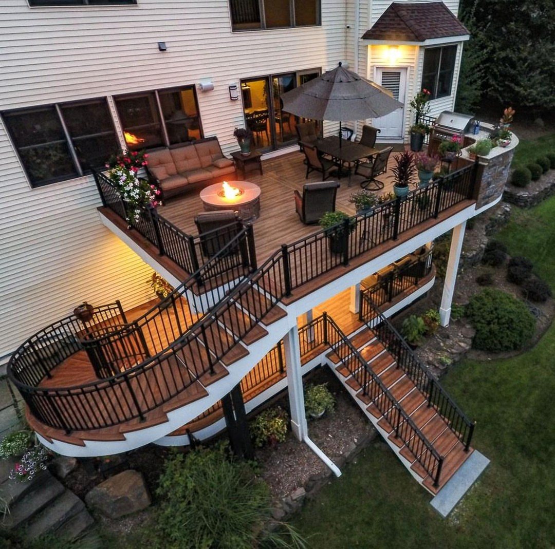 Elevated wooden deck with curved stairs, outdoor furniture, and a glowing fire pit at dusk.
