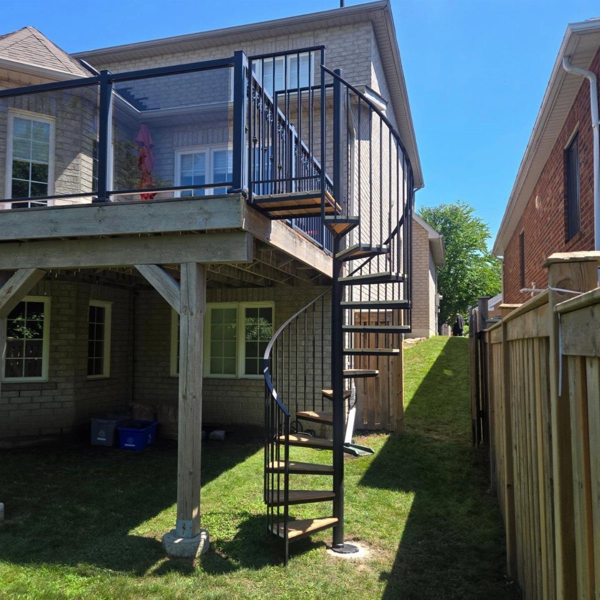 A black metal spiral staircase connecting an elevated wooden deck to a green grassy backyard.