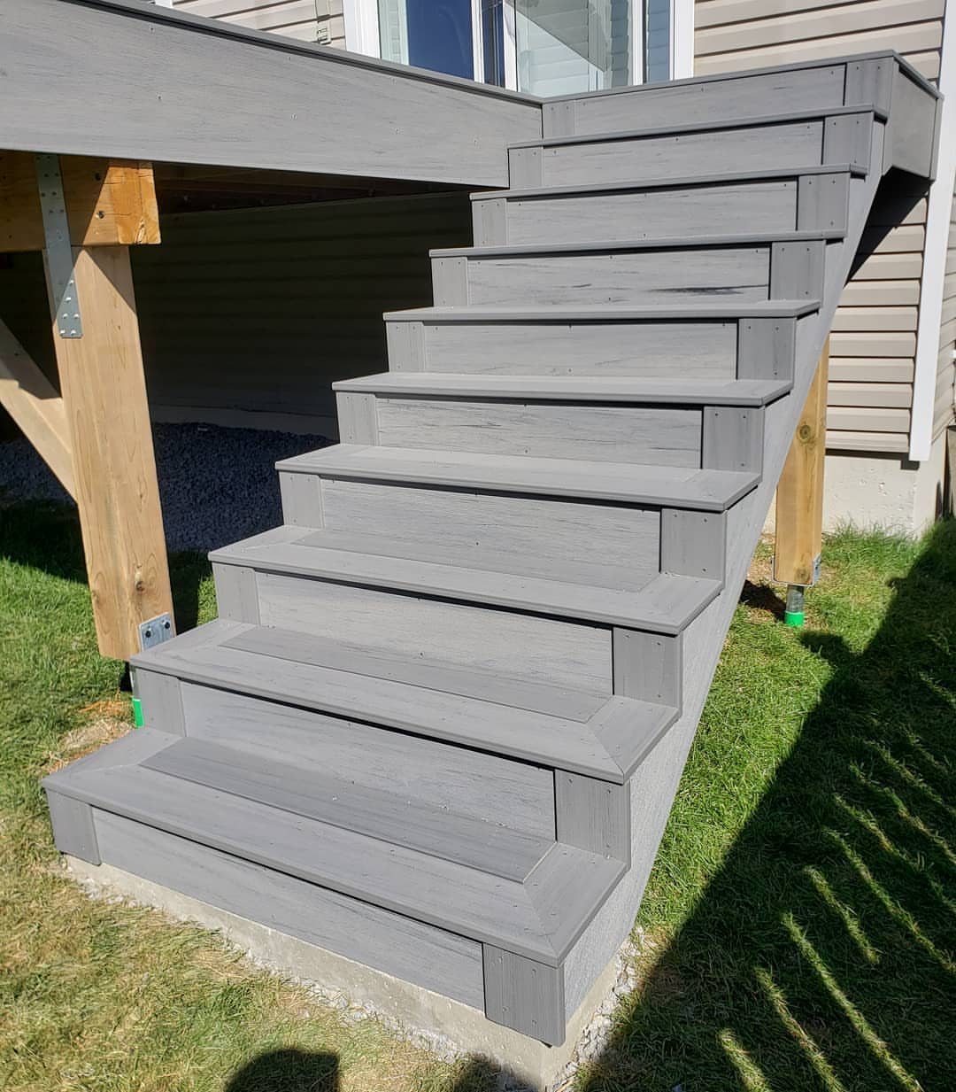 Grey wooden deck stairs leading from a raised platform down to a green lawn.