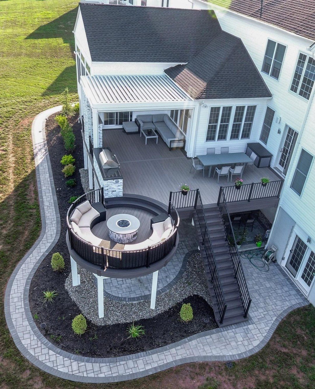 A multi-level wooden deck featuring a circular lower section with a central fire pit and built-in seating.
