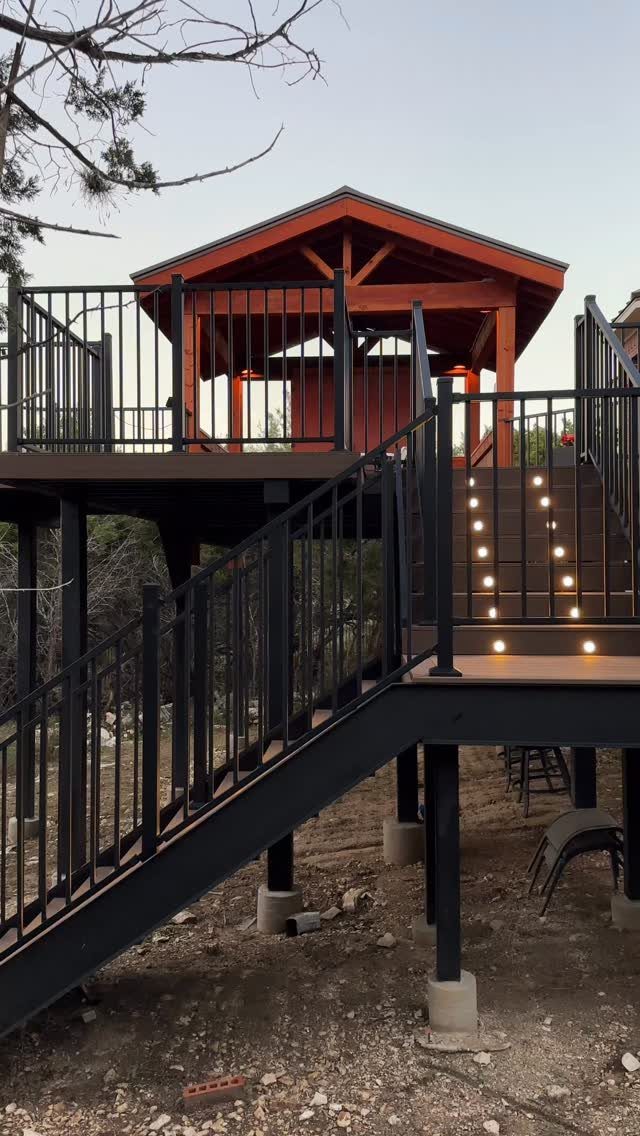 Elevated dark wooden deck with black metal railings, stairs, and a wooden gazebo structure.