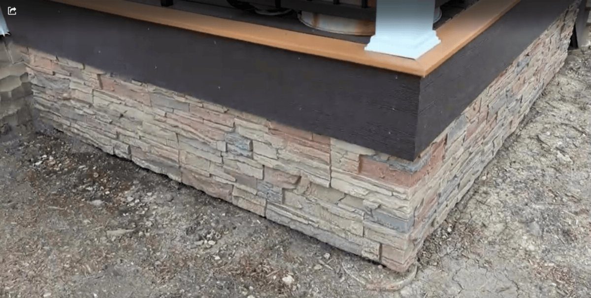 Faux stone skirting in tan and grey tones installed along the base of a wooden deck.