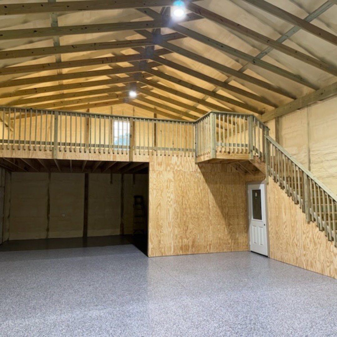 Interior of a wooden pole barn garage showing a loft space with railings and a staircase.
