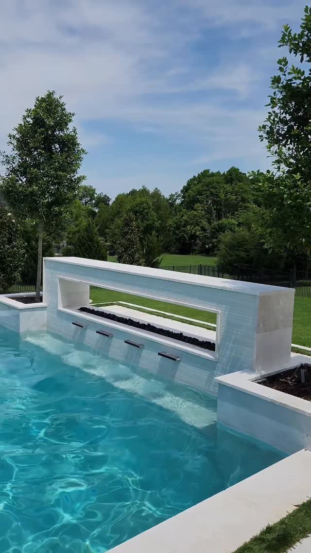 A white stone fire feature trough built into the edge of a swimming pool.