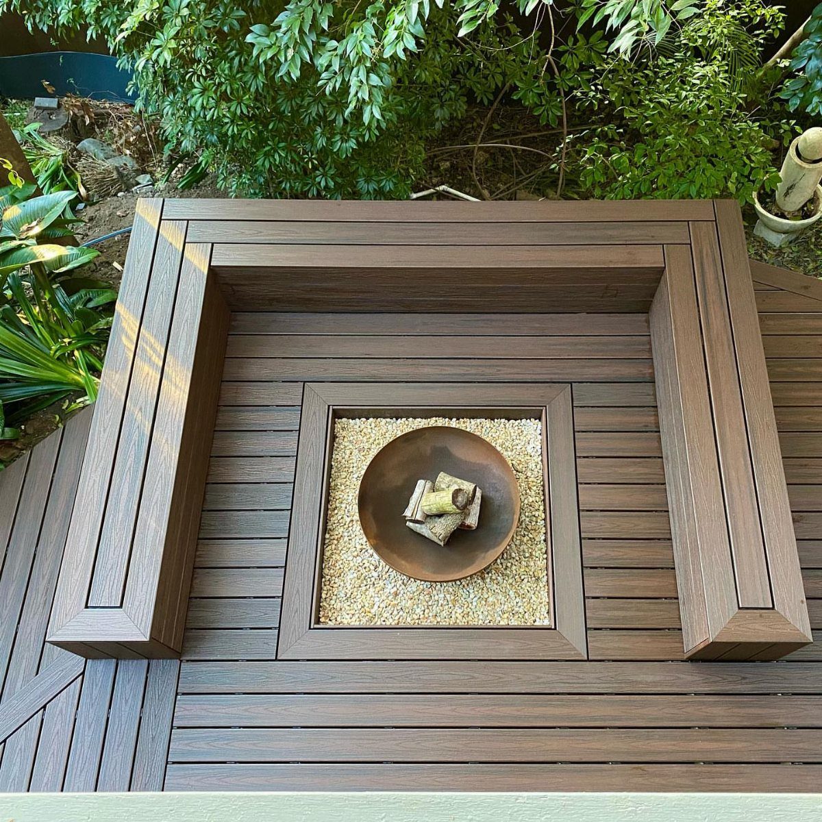A built-in wooden deck fire pit with a metal bowl and wood pieces.
