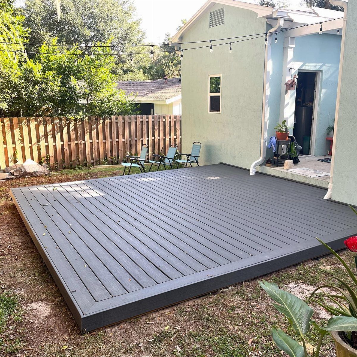 A dark grey floating wooden deck installed on a grassy backyard lawn next to a house.