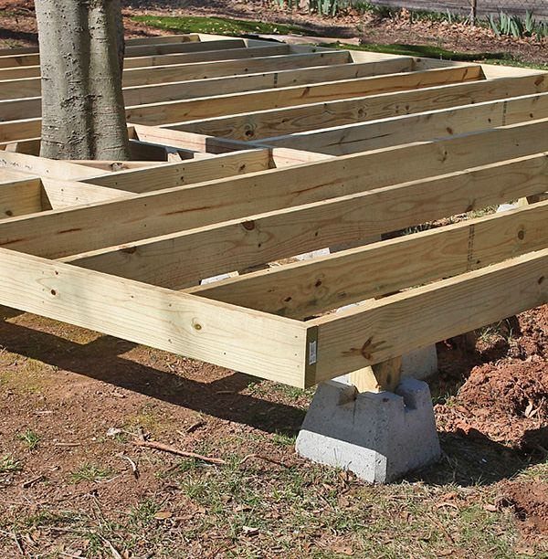 Wooden deck framing under construction supported by concrete blocks on the ground.