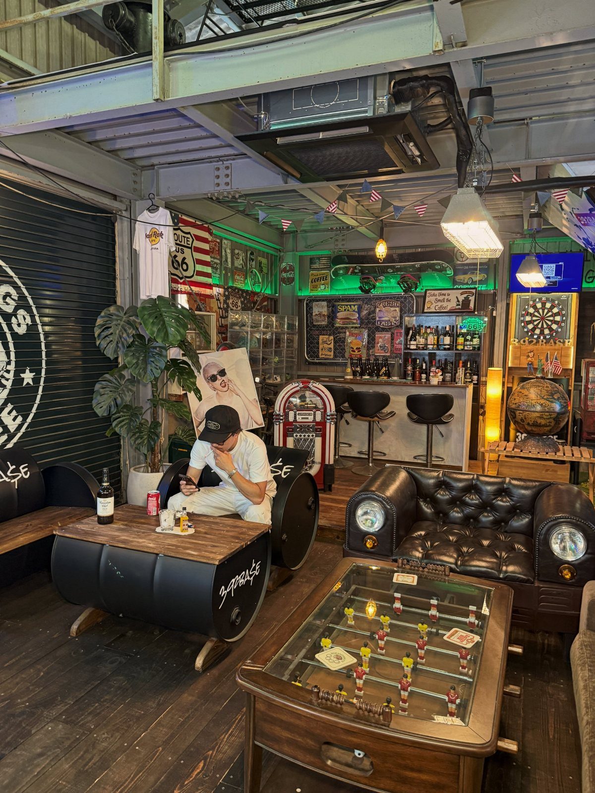 A decorated garage man cave featuring a bar, foosball table, and car-themed leather sofa.
