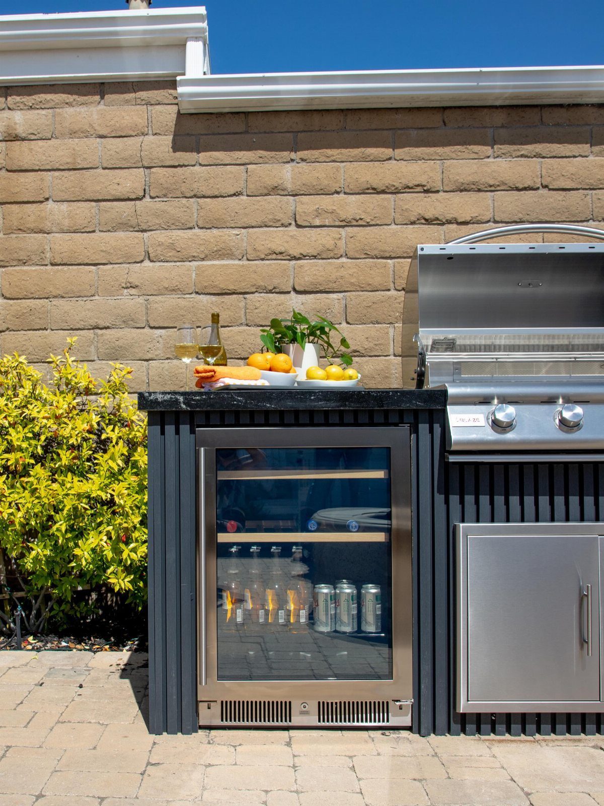A built-in beverage cooler with glass door sits within a black outdoor kitchen island.