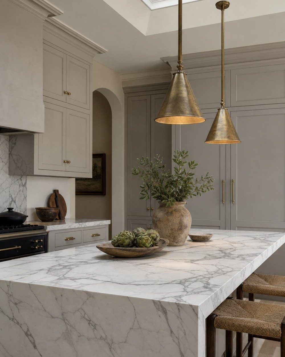 Two brass conical pendant lights hanging above a white marble kitchen island.