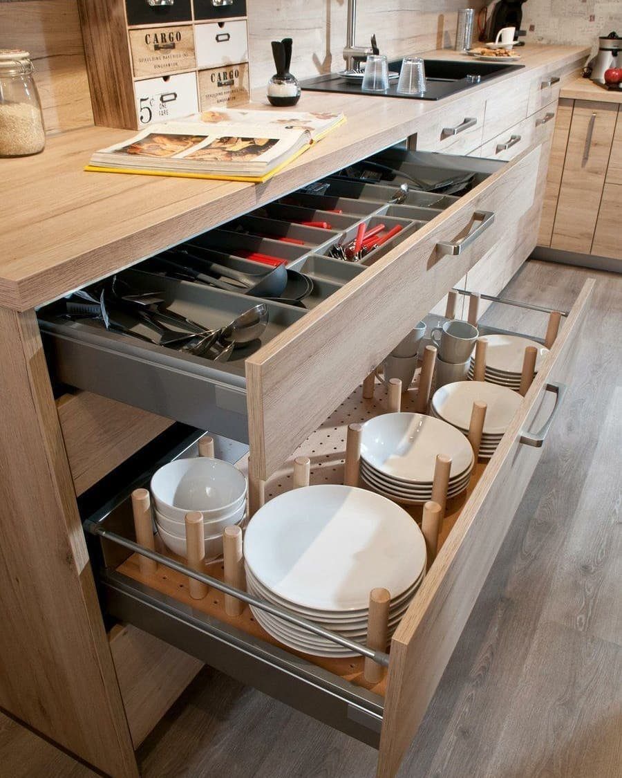 Open light-wood kitchen drawers with grey organizers holding plates, bowls, and utensils.