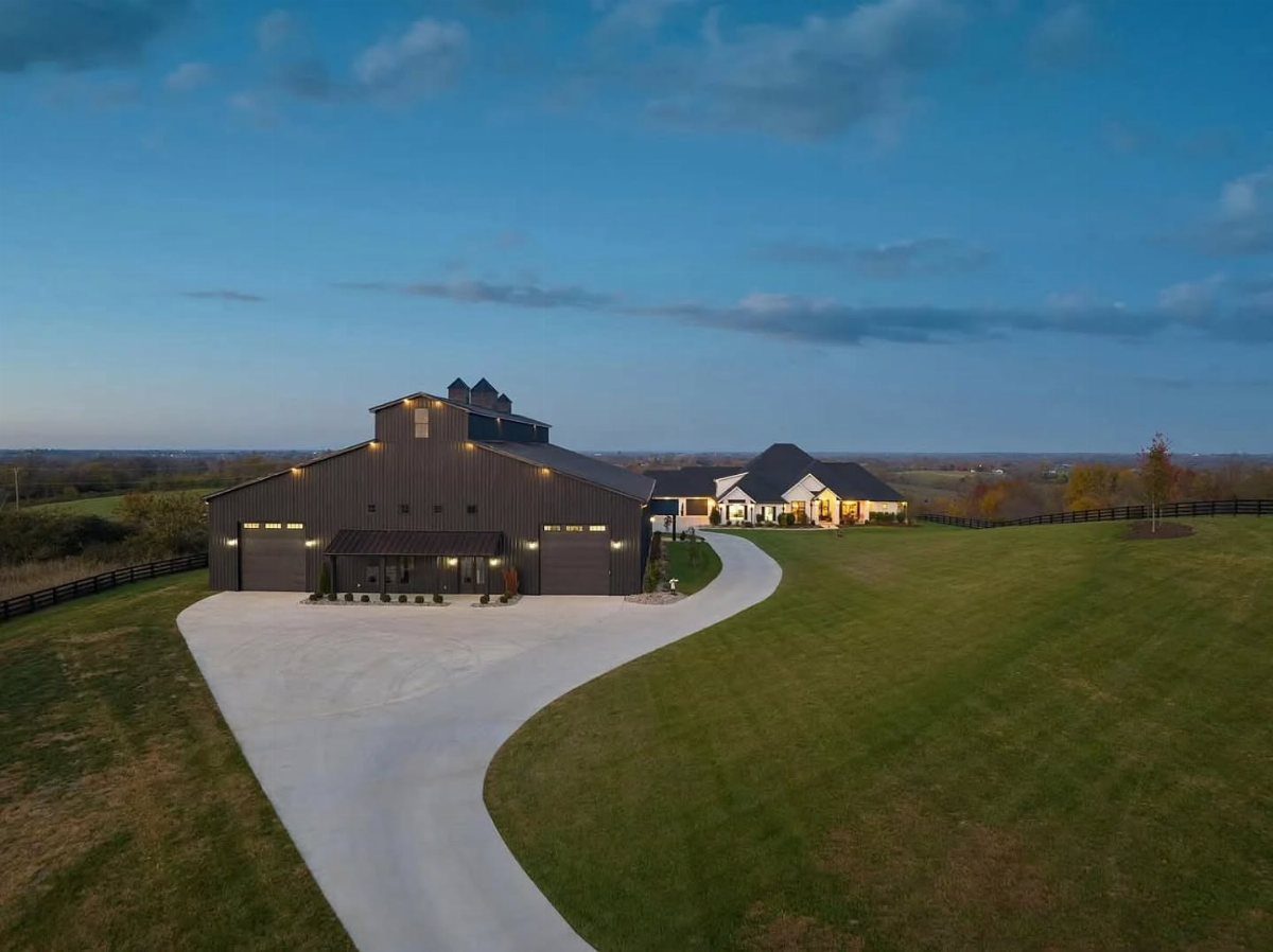 Large dark barn-style garage with multiple bays and a long white driveway on a green lawn.