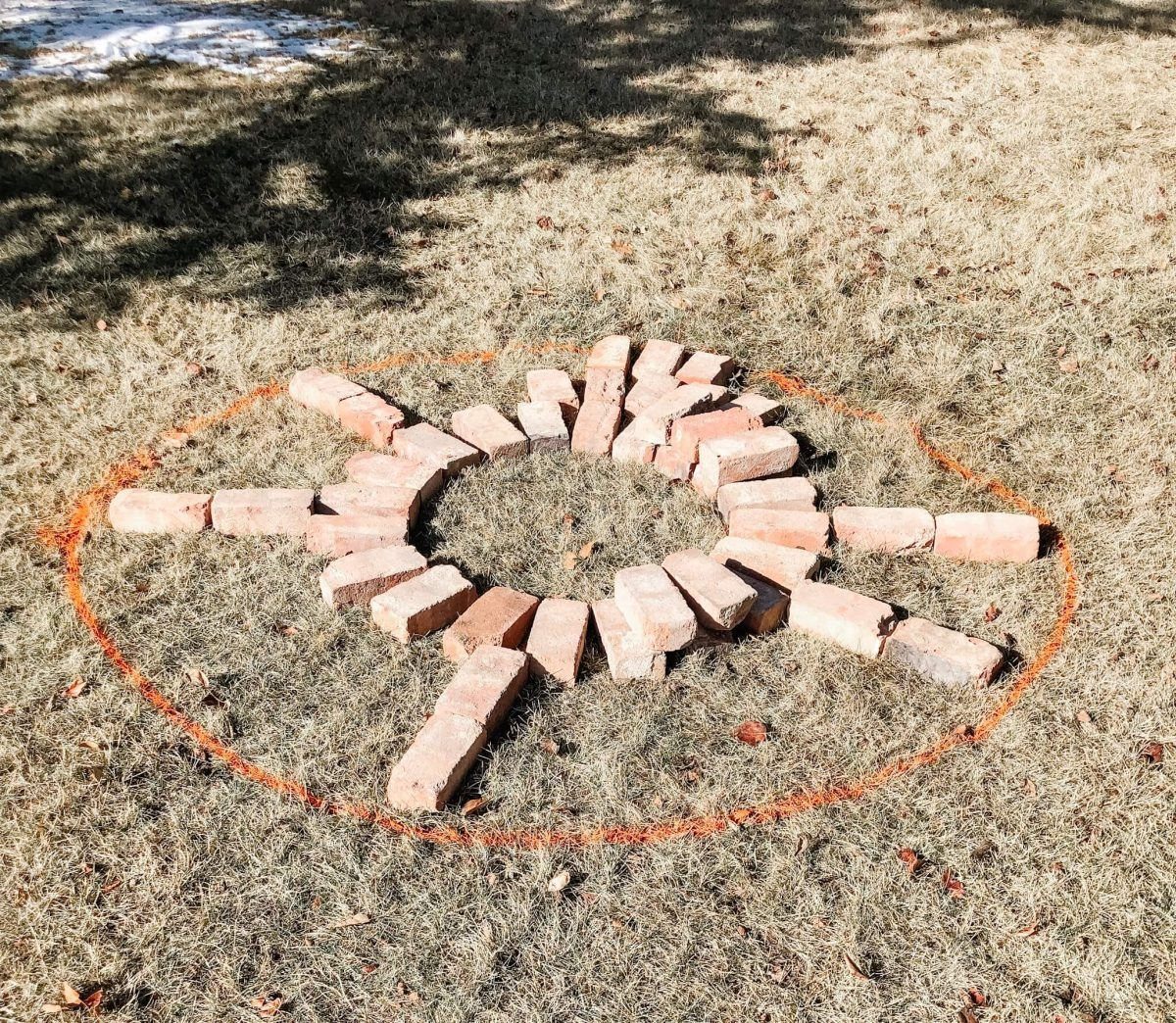 Bricks arranged in a circular pattern on grass with an orange spray-painted outline.