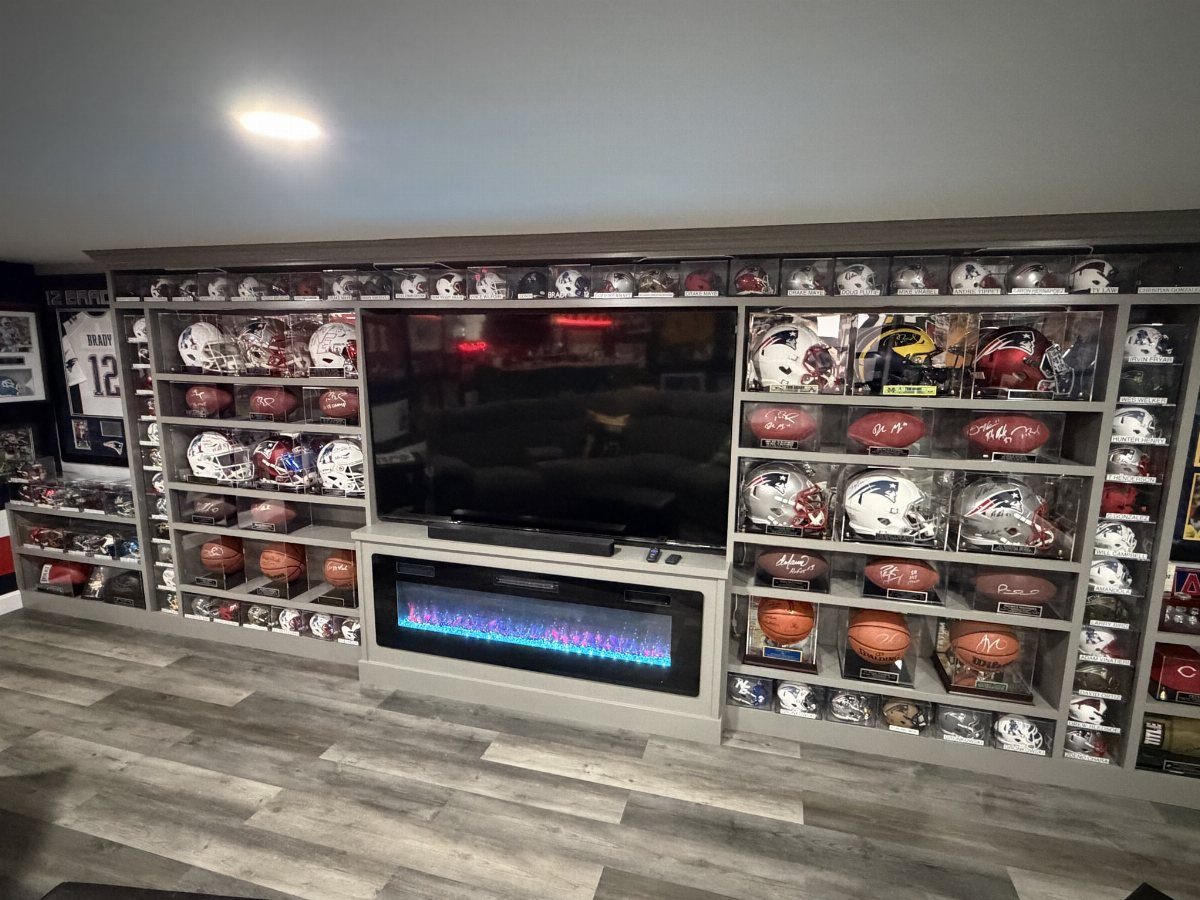 Grey shelves displaying various football helmets and footballs surrounding a large television and electric fireplace.