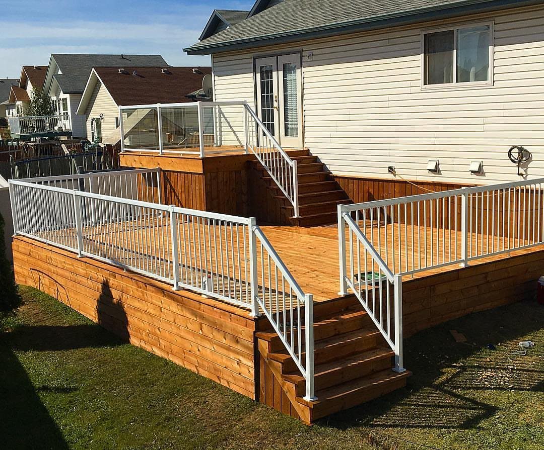 A large two-tier wooden deck with white railings and stairs attached to a house.