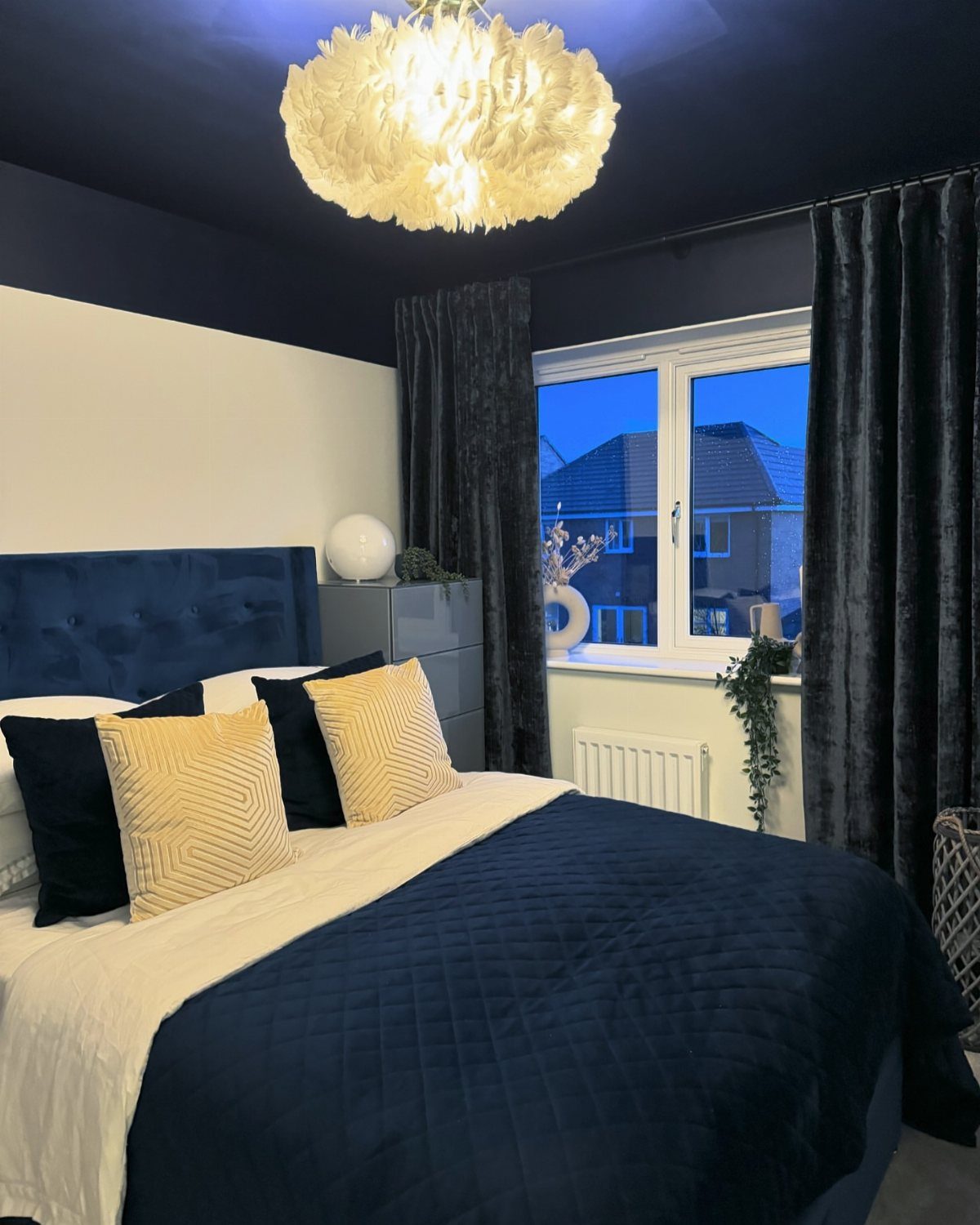 Navy blue curtains in a bedroom with matching bedding and a fluffy ceiling light.