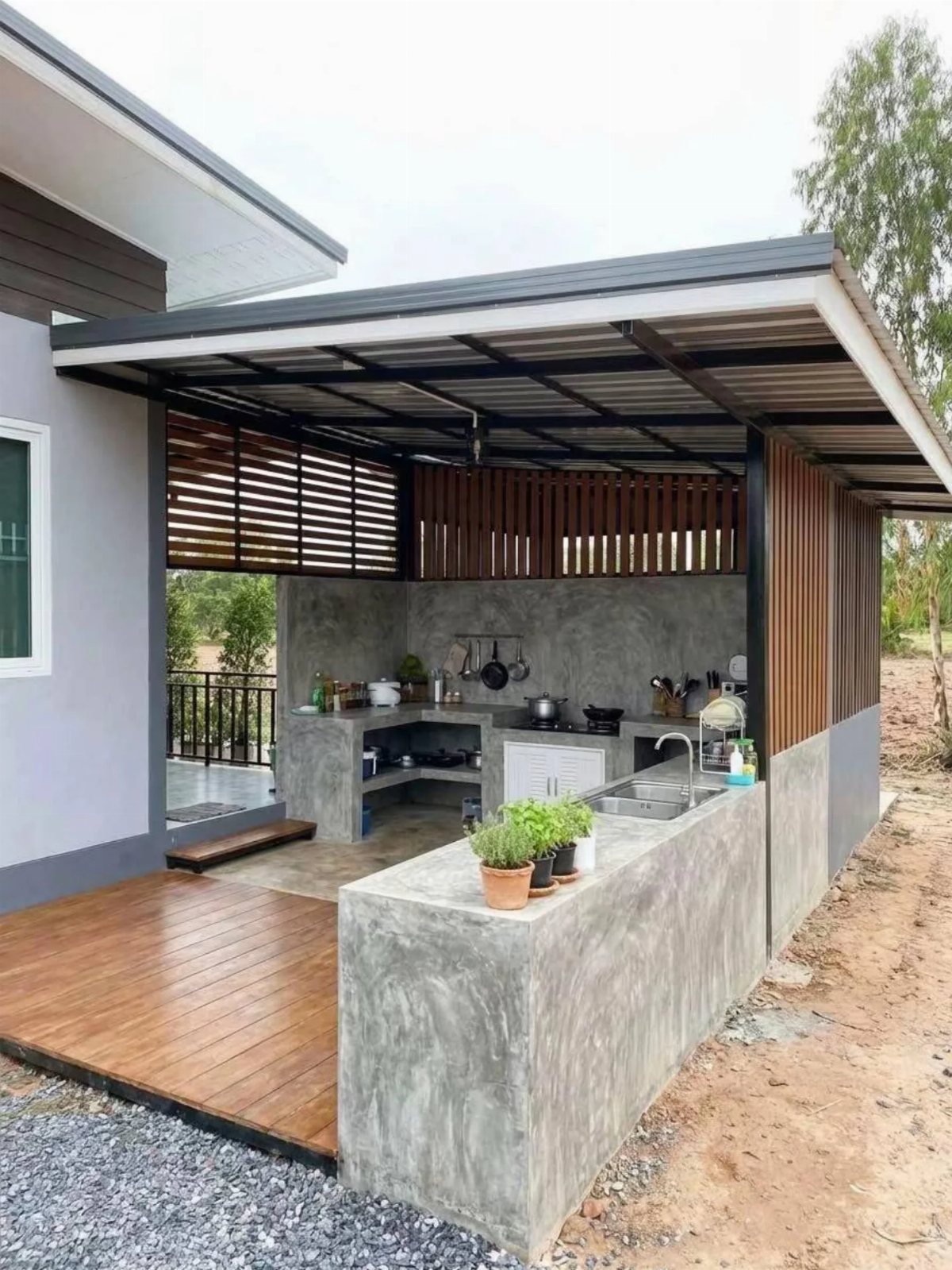 Modern concrete outdoor kitchen with a sink and stovetop under a dark metal roof structure.