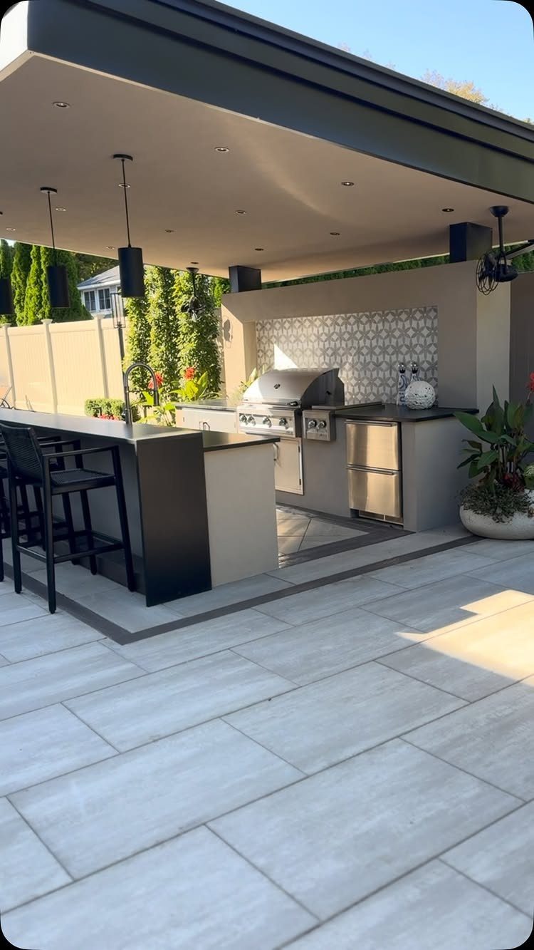Modern outdoor kitchen with stainless steel appliances, a black bar counter, and grey stone patio tiling.