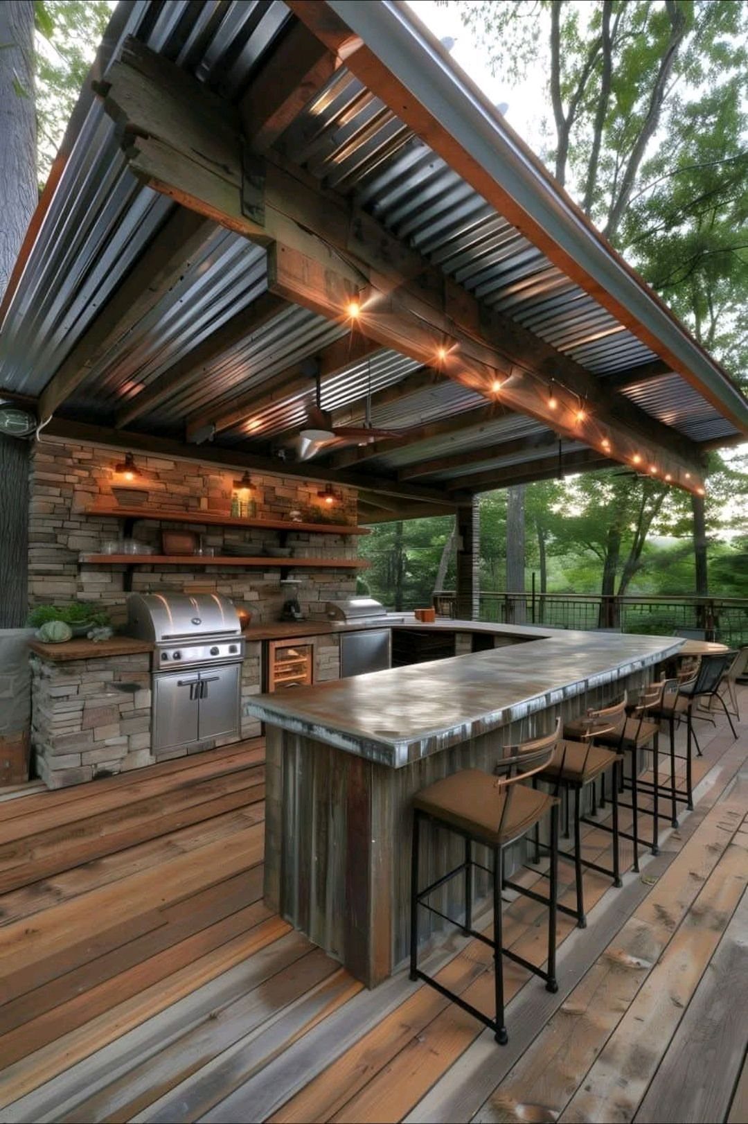 Rustic outdoor kitchen with stone walls, stainless steel grill, and a long concrete bar on a wooden deck.