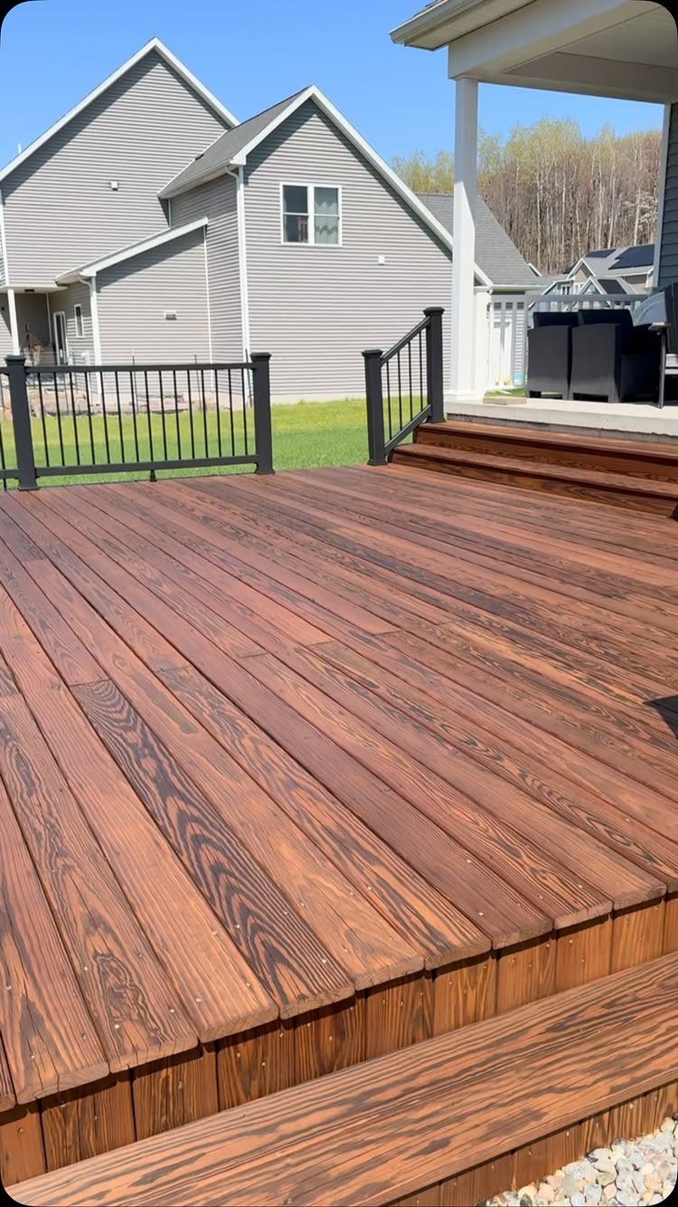 Stained wooden deck with dark brown finish and black metal railings in a backyard setting.