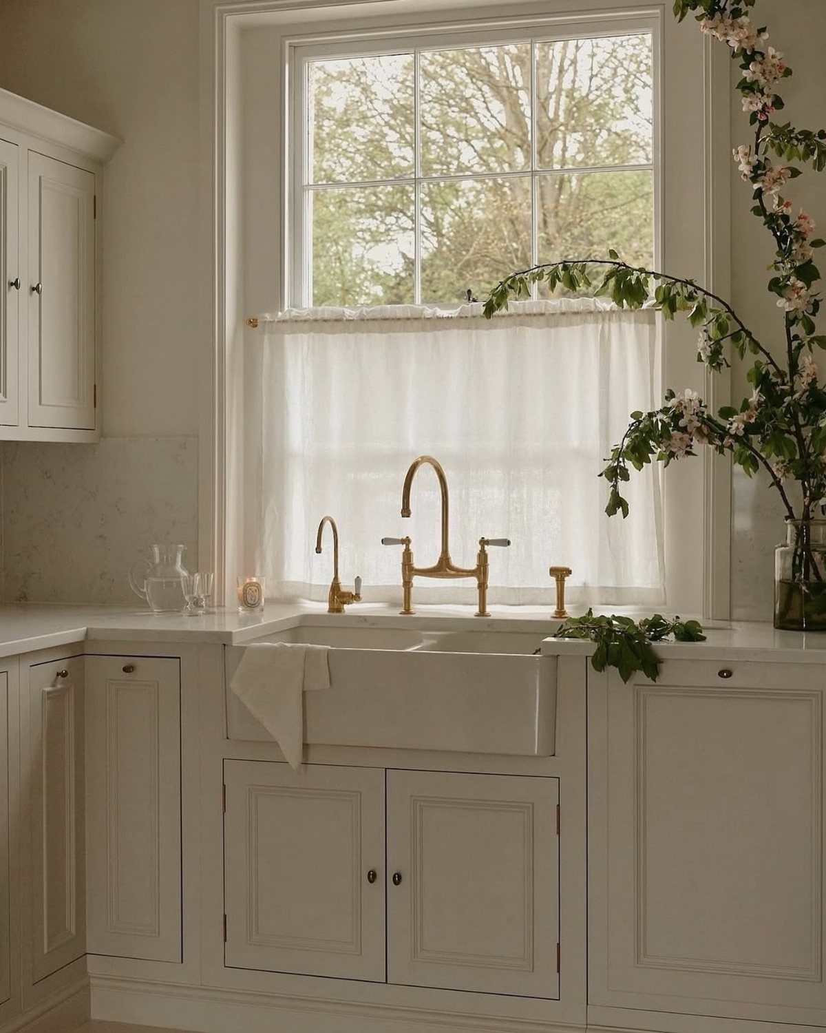 Gold bridge faucet on a white farmhouse sink in a bright kitchen.