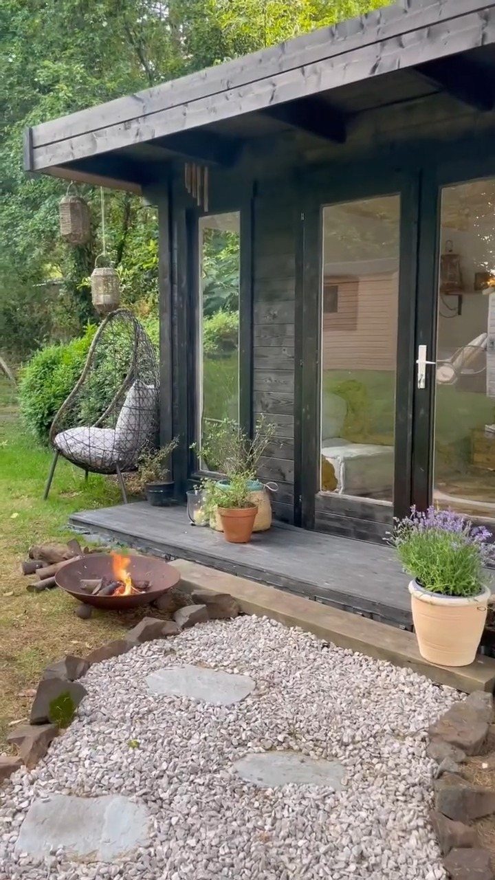 A dark wooden garden shed with glass doors and a small integrated porch area.