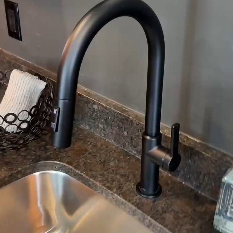 Matte black pull down kitchen faucet installed on a brown granite countertop.