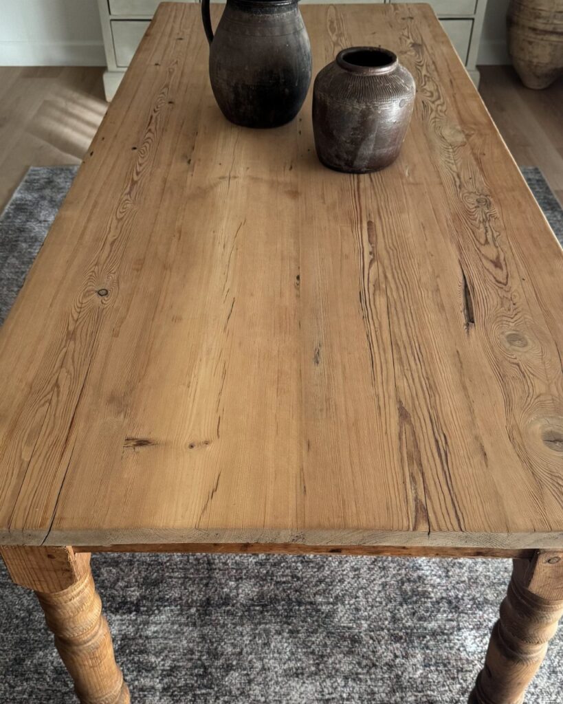 Rustic wooden dining table with two dark ceramic vases on a grey rug