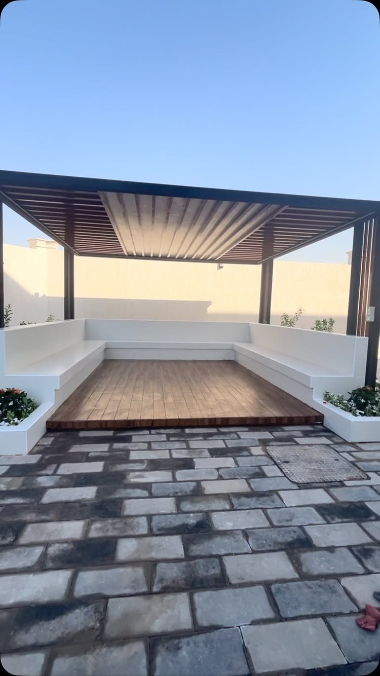 A wooden deck with built-in white benches under a pergola adjacent to a stone patio.