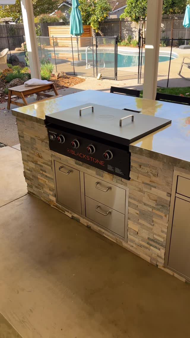 A smooth concrete countertop on an outdoor kitchen island with a built-in griddle and stone base.