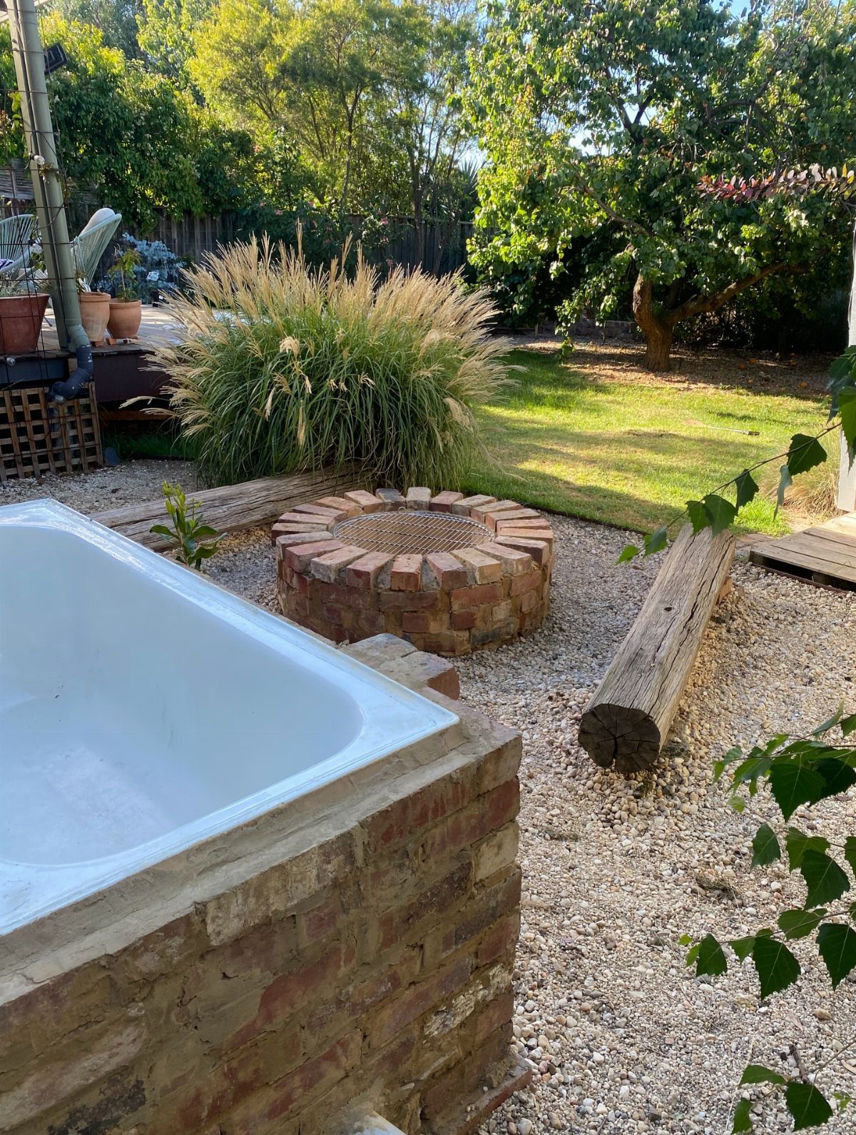 A circular brick fire pit constructed with staggered brick layers on a gravel backyard surface.
