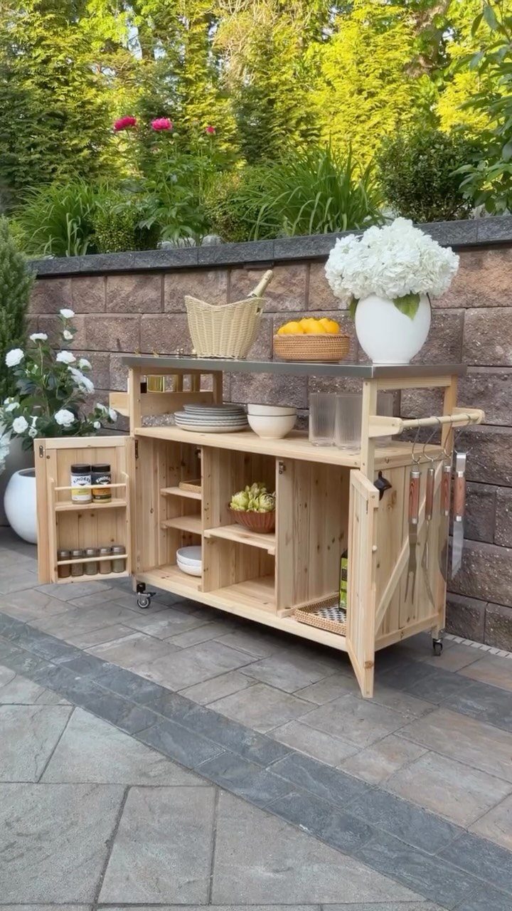 Wooden mobile kitchen cart with open shelves and cabinets on a stone patio.