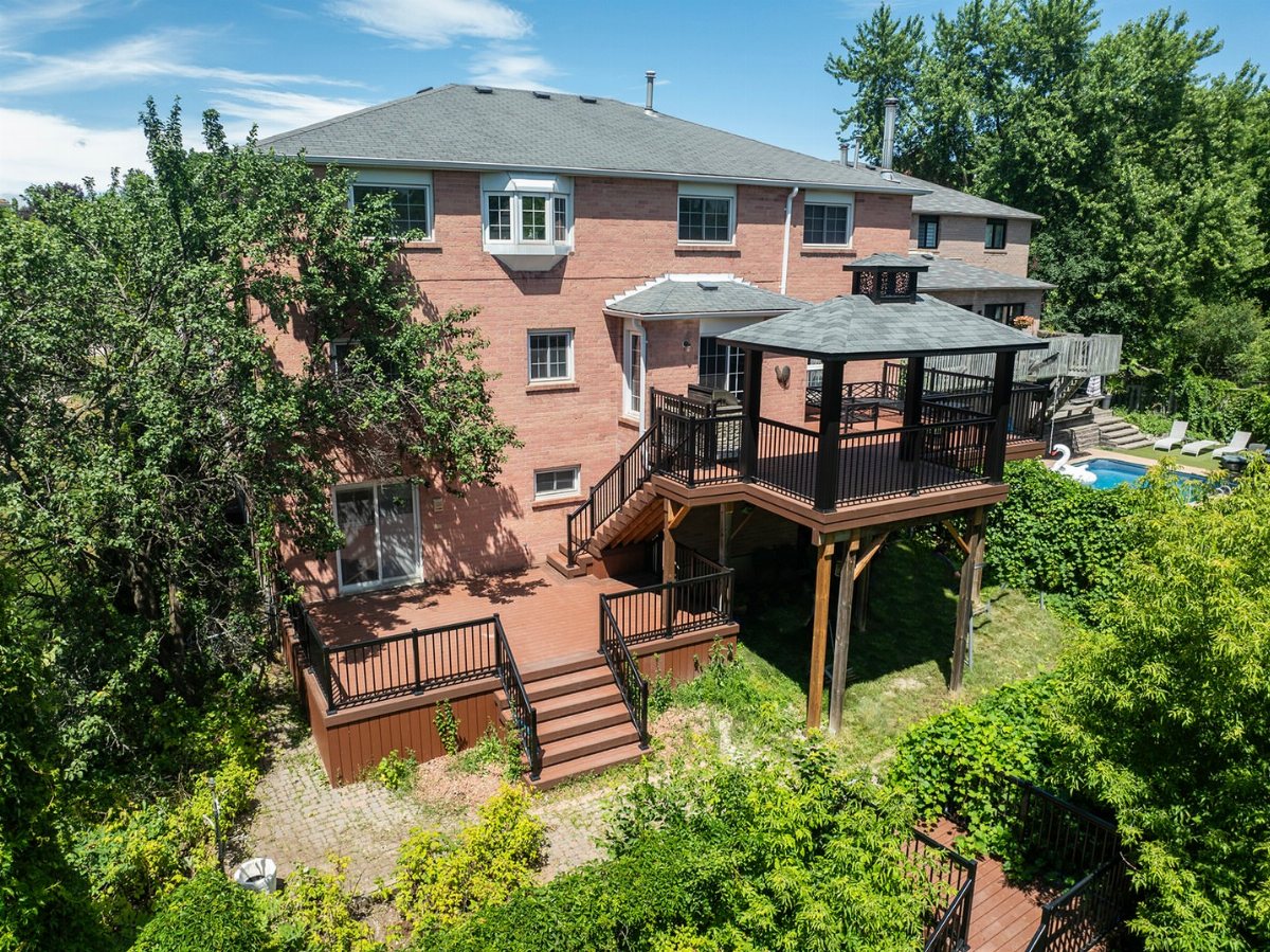 A multi-level wooden deck with a covered gazebo attached to a large brick house.