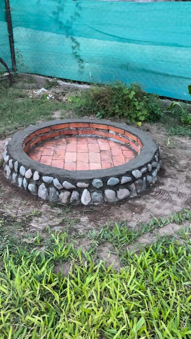 A circular fire pit made of red bricks and grey stones in a garden.