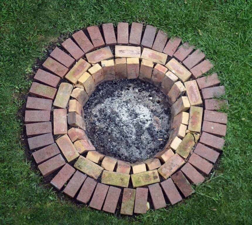 A circular brick fire pit with light inner bricks and dark outer bricks on grass.